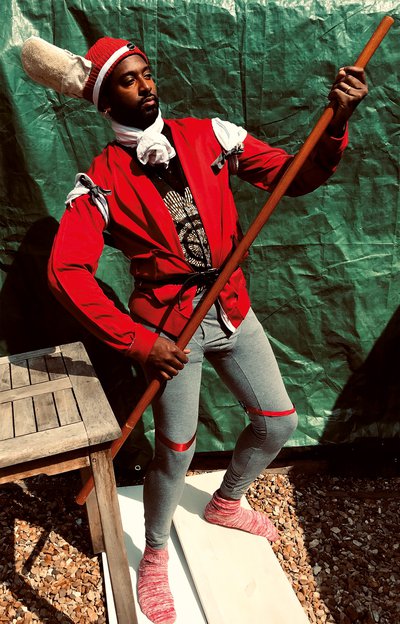 Brathwaite wearing grey trousers, red jacket and red cap, holding wooden pole as if propelling a gondola